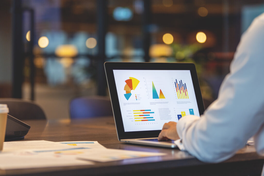 Een persoon zit aan een bureau, gefocust op zijn laptop, terwijl hij gegevens bekijkt en analyseert met behulp van performance monitoring software. Naast de laptop liggen aantekeningen en een grafiek die trends in de prestaties laat zien. Zo kan hij vroegtijdig signaleren wanneer er iets mis gaat, om verstoringen te voorkomen.